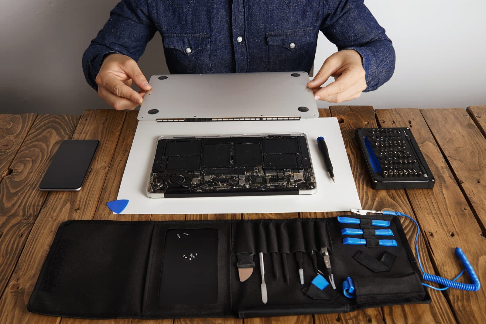 A technician opening the back cover of a laptop on a workbench