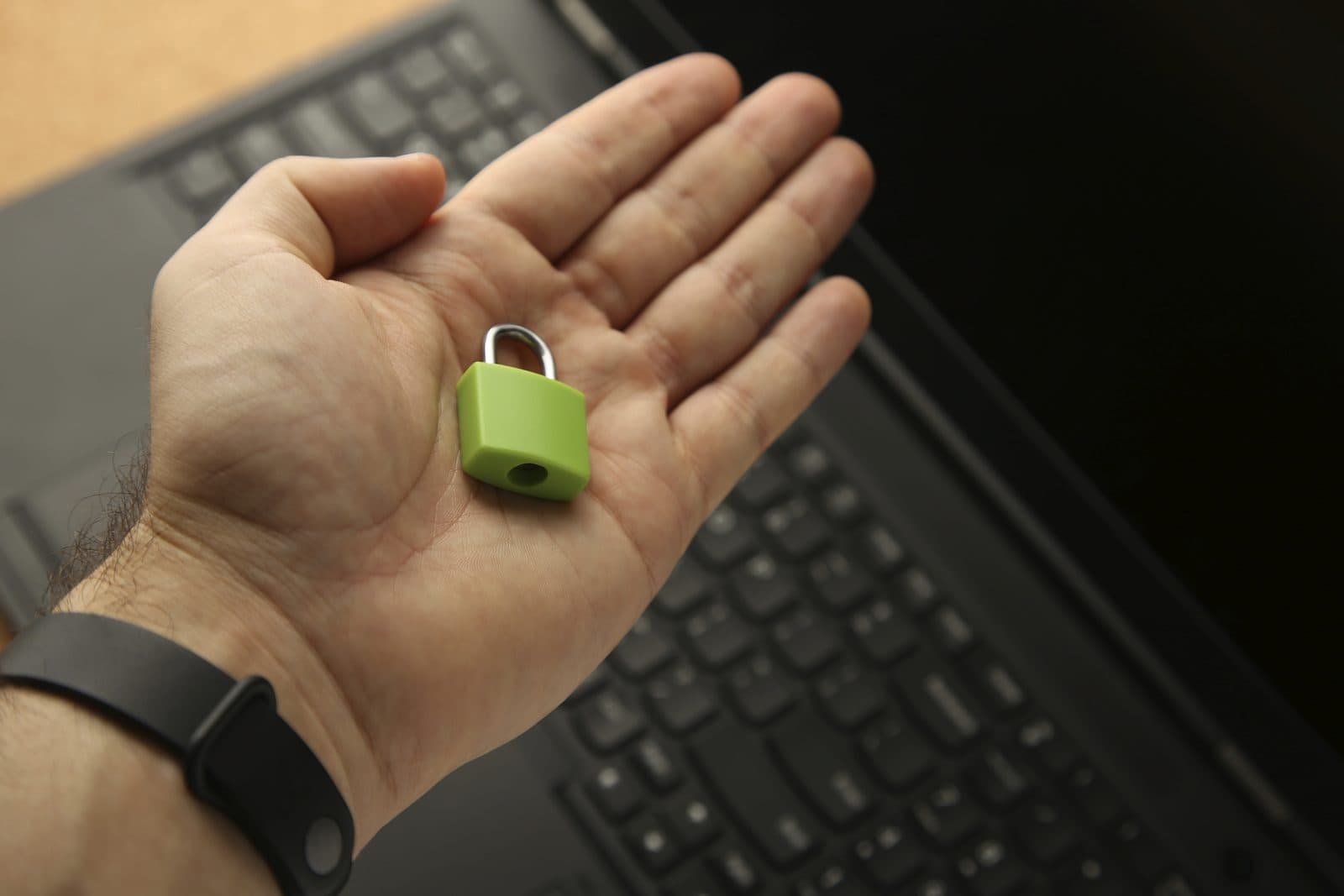 A hand holding a green padlock in front of a laptop keyboard