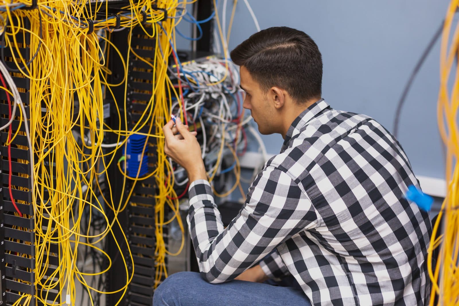A network engineer working on a patch cabinet full of cables